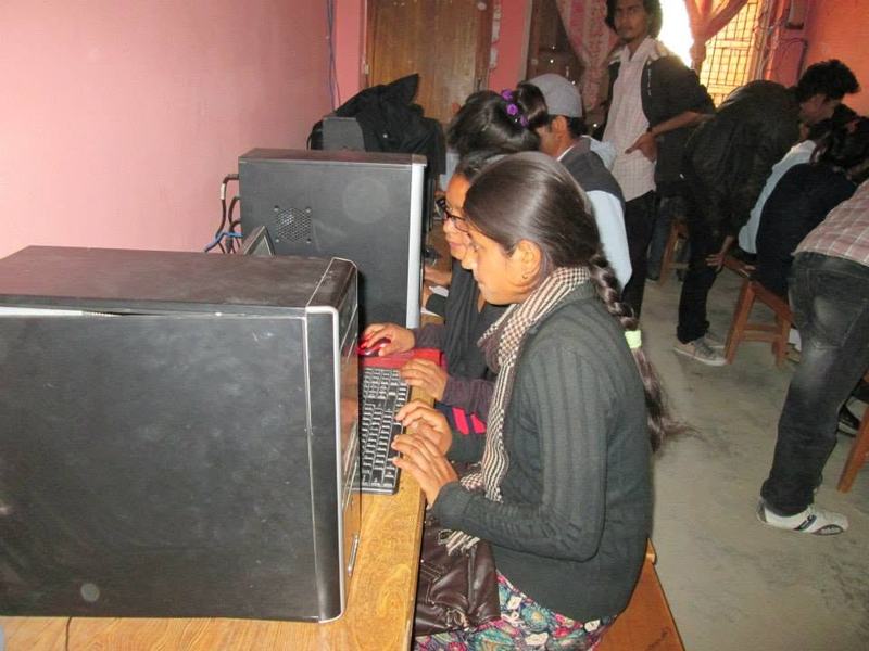 A young woman types at a desktop computer in a crowded school computer lab