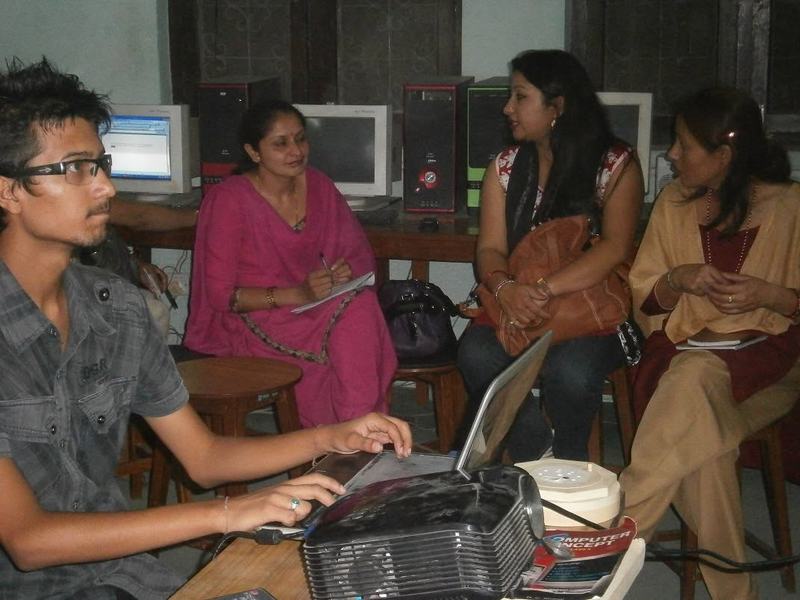 Teachers with notebooks sit beside a trainer using a laptop and projector