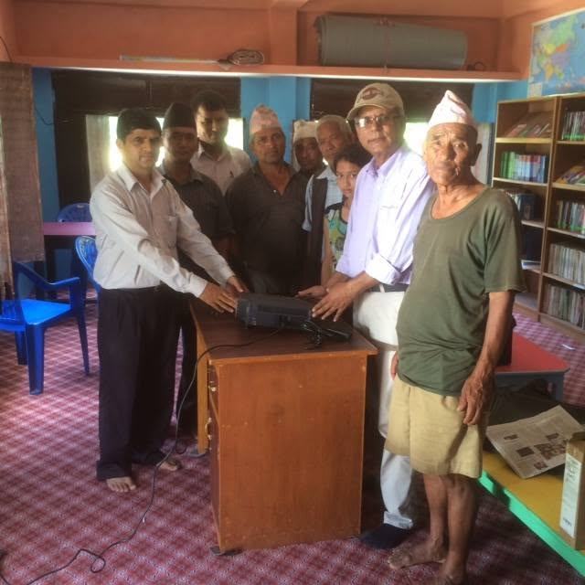 Community members and school staff gather around a table as equipment is handed over in a library