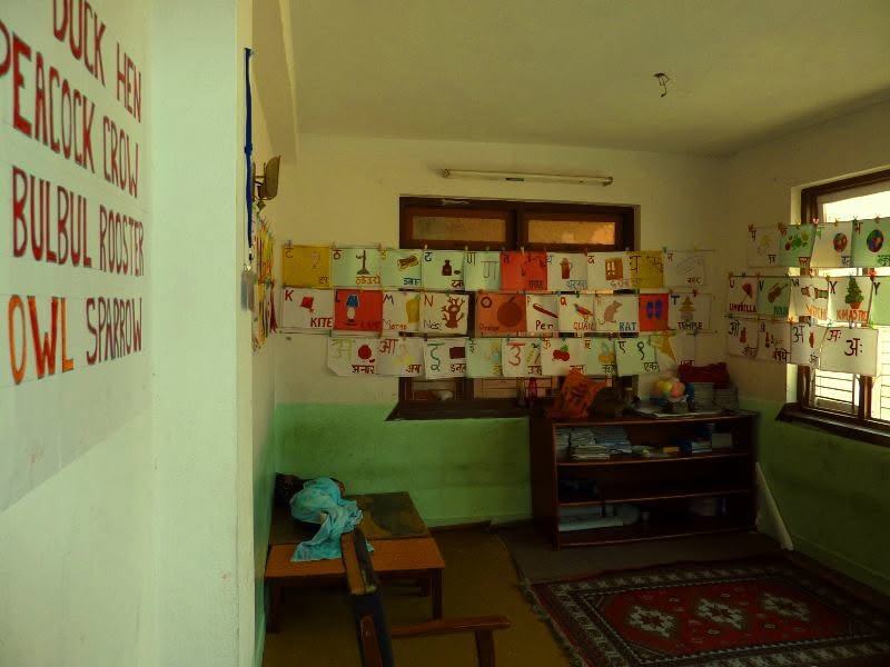 A classroom reading space with children’s artwork on the walls and alphabet words painted on a wall